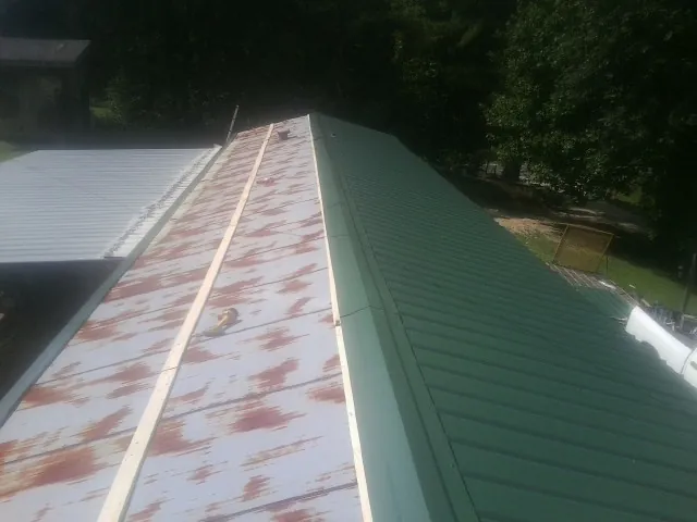 Old rusted panels beside newly installed green metal roofing — Wind Damage Roof Repair by Roofing Brothers in Minot