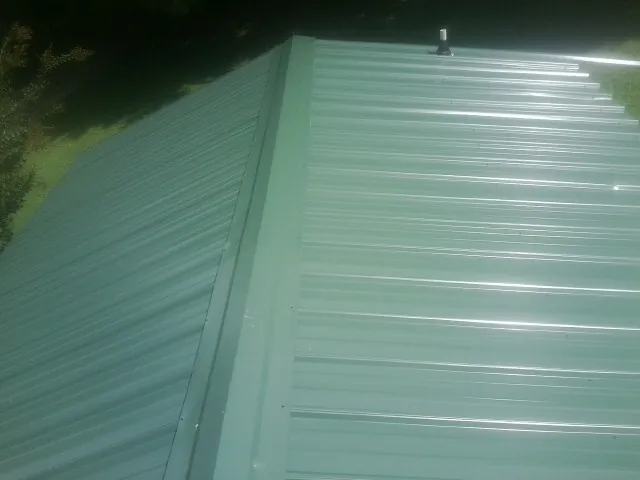 New green metal panels meeting at the ridge of a roof — Flat Roof Repair work by our crew in Minot
