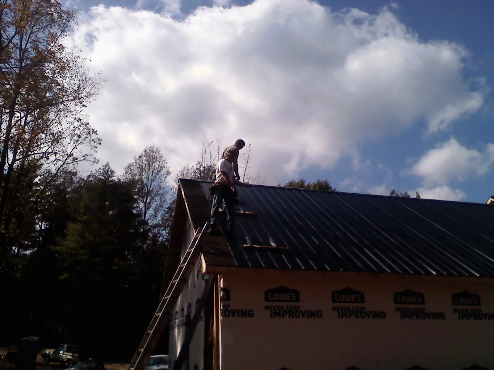 Roofer fastening dark metal panels high against a cloudy sky, from a Roof Inspection job in Minot