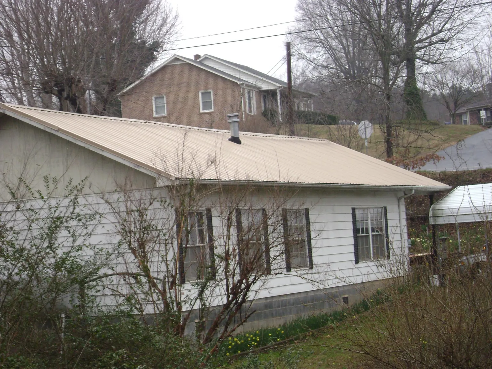 Tan metal roof on a white sided house set into a hillside — Commercial Roofing by Roofing Brothers in Minot